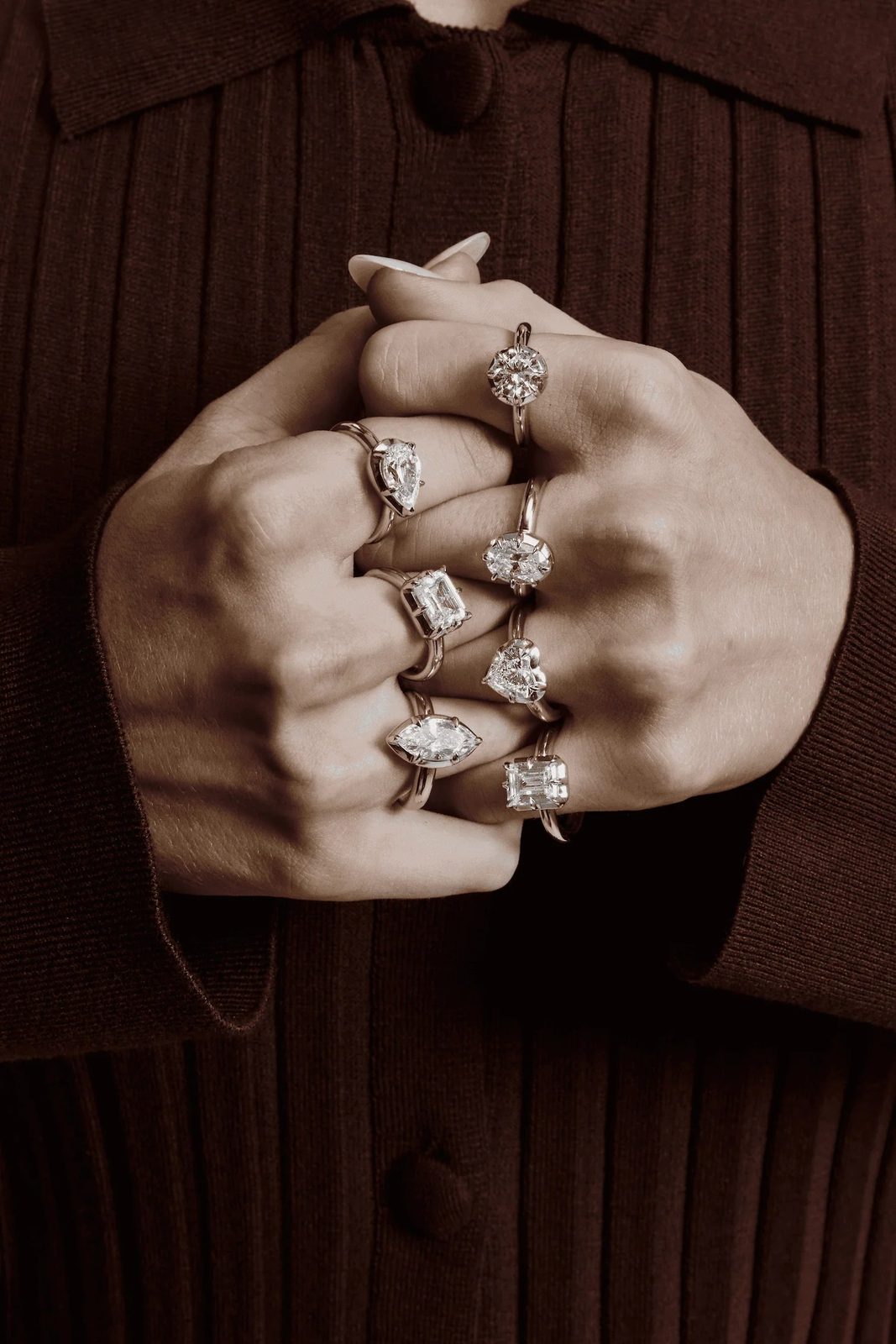 Clasped hands wearing seven solitaire rings in different diamond cuts