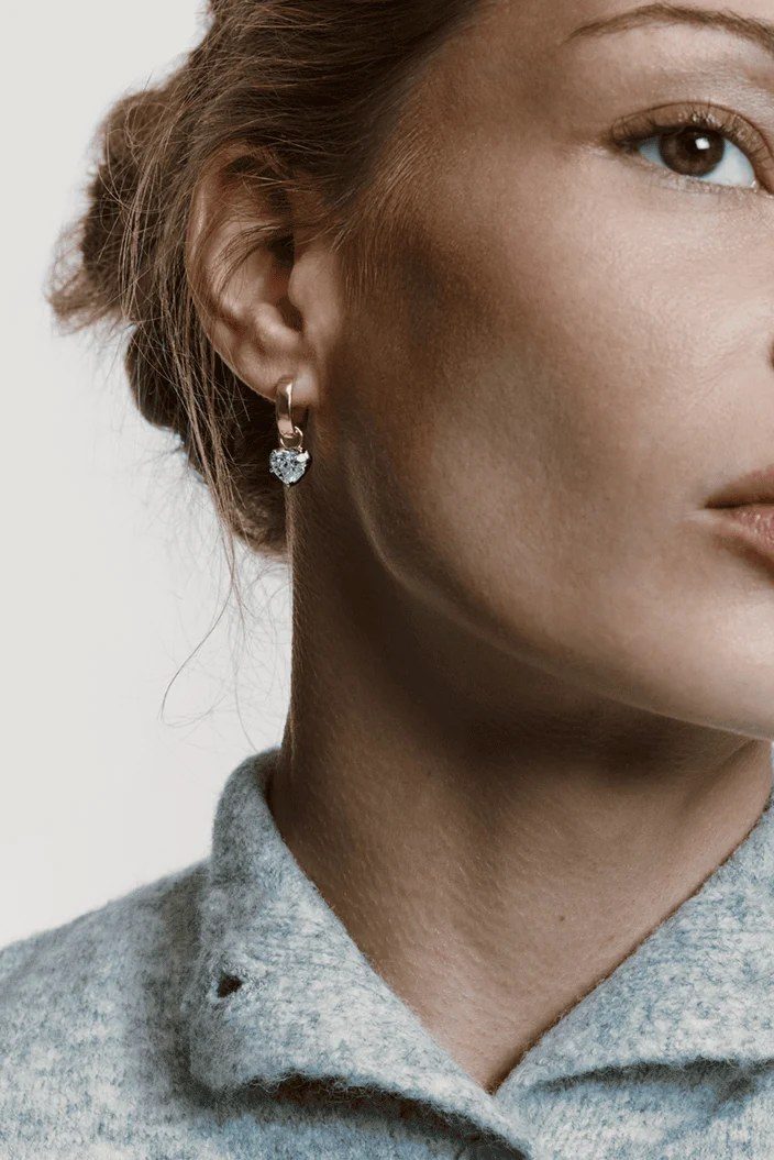 A woman wearing a gold hoop earring with a heart-cut drop
