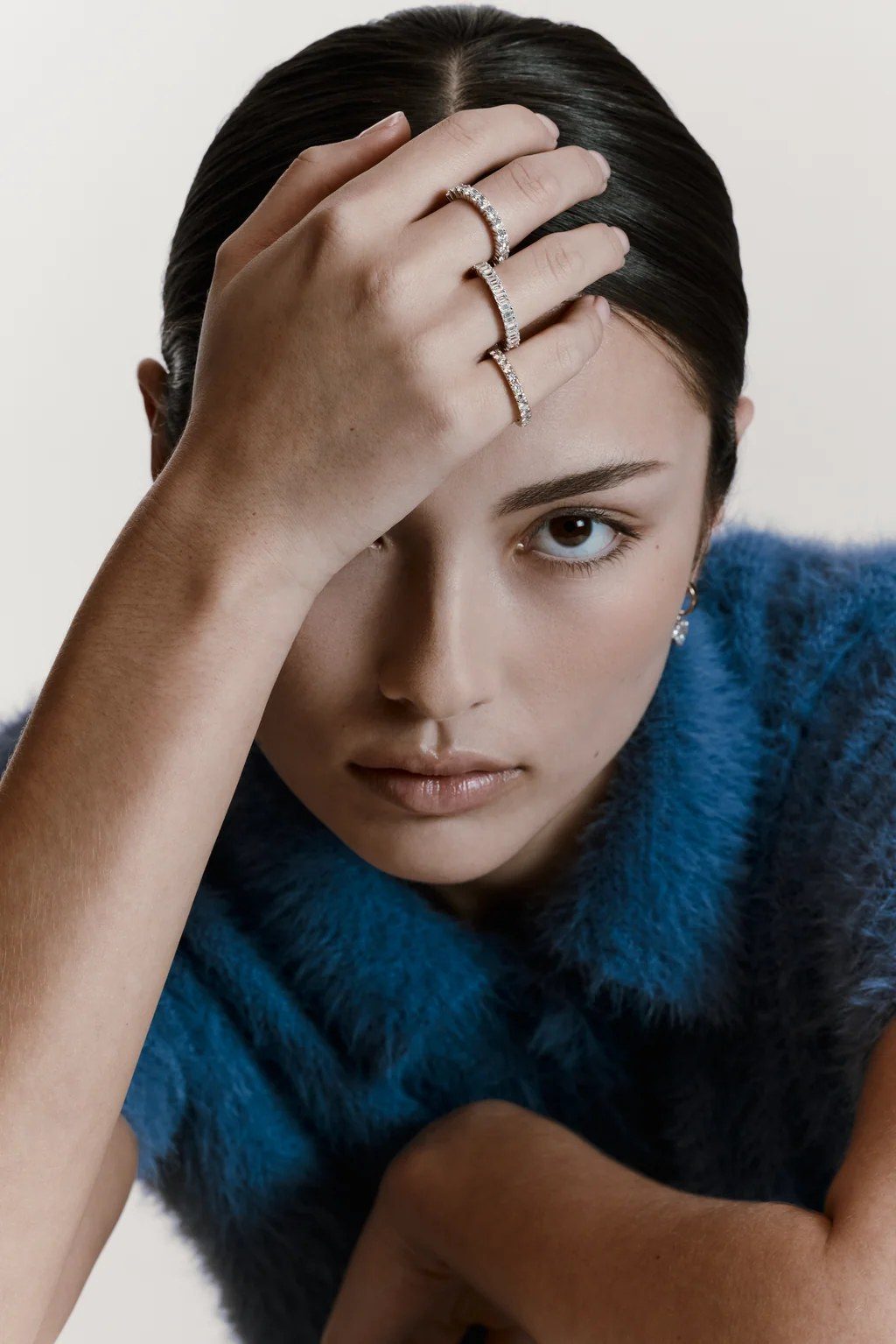 A woman resting her hand on her forehead, wearing three stacked diamond bands